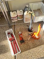 Overall lot on garage floor: hydraulic pump, jack handles in tray, funnels, chemical jugs on shelf