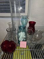 Group shot of all ten glass vases and jar on wire shelf