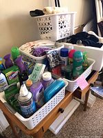 Overall view of three white baskets on table containing assorted cleaning products and towels; foam cooler visible