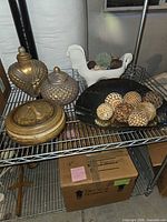 All items on metal shelf: two brown-gold lidded jars, dark scalloped bowl with decorative spheres, white ceramic animal planter