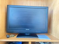 Front view of Dynex LCD TV on stand with remote, manual visible