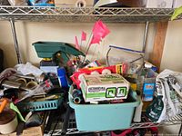 Shelf with spreader, flags, box of walkway lights, tote of hose parts, torch fuel, soil bag