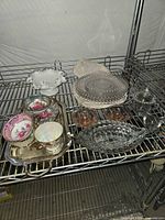 Overview of all items on shelving: Candlewick plates, sugar, creamer, teacups on metal tray, white milk-glass bowl
