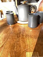 Teapot on wood trivet with three of the four cups visible