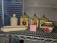 All items on metal shelf: cream canister, four Olive & Thyme canisters, music box, two plates