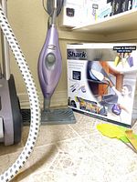 Steam cleaner with cord, mop head, box and accessories on floor
