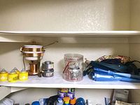 Shelf with copper warmer, fuel cans, Slatkin & Co cylinder, yellow canisters, blue plastics, fabric bags