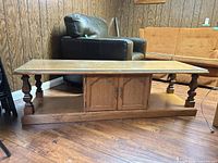 Front angled view of entire coffee table showing glass top, storage doors, legs, shelf