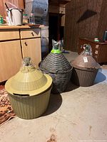 Three demi-johns standing side by side on basement floor