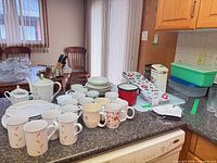 Wide view of entire lot on countertop including porcelain set, mugs, enamel mug, cutting board, trays, Tupperware and bin