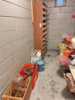 Basement corner with carboy in wooden crate, red crate with bottles, bucket, wine rack in background