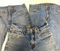 Three pairs of men’s blue jeans laid flat showing waistbands and front fly areas