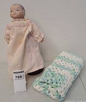 Doll standing on stand next to folded blanket showing overall items