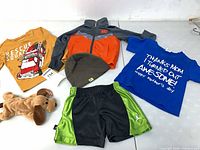 All six items laid out: Nike jacket, beanie, two T-shirts, Jordan shorts, plush dog