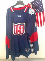 Front view of navy Adidas Team USA WCH 2016 jersey with USA crest and attached small USA flag