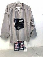 Grey LA Kings hockey jersey hanging with two unopened packs of hockey laces beneath