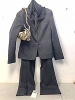 Full view of black pant suit, scarf, and gold handbag