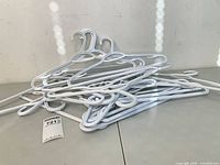 Pile of 18 white plastic clothes hangers on tabletop