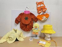 All items arranged: romper, diaper cover, booties, hand-knit sweater, sun hat on form, bib, plush chick