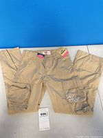Full view of khaki cargo slacks laid flat showing overall style and tags