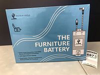 Front of sealed retail box "The Furniture Battery" by the blue cactus