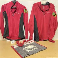 Two maroon/black quarter-zip jerseys and grey Roots tote displayed on table