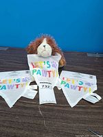 Stuffed dog plush centered behind two packaged “LET’S PAWTY!” bandanas on table