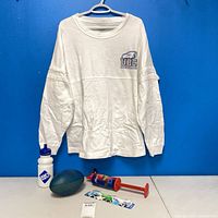 Front view of white UBC Thunderbirds long sleeve shirt on hanger with accompanying football, water bottle, air horn and lanyard displayed