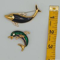 Both dolphin brooches beside tape for scale