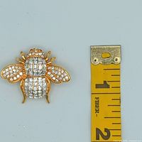 Front view of Joan Rivers bee brooch next to measuring tape showing size