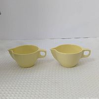 Front view of two pale yellow melamine creamers