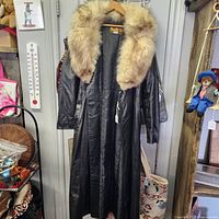 Front view of black leather coat with fur collar hanging