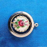 Front view of round pendant showing floral cross-stitch inside metal frame