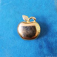 Front view of gold-tone apple brooch on blue fabric