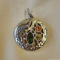 Front view of pendant showing silver-tone openwork design and three coloured glass rhinestones