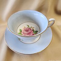 Teacup resting on saucer showing rose motif and gilt trim