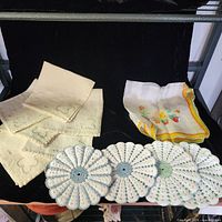 Stack of embroidered napkins, crocheted pot holders/doilies, printed handkerchief visible