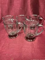 five clear glass handled goblets with ruby red feet grouped on red background