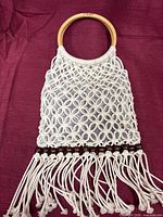 Front view of cream macramé handbag with wooden handles and fringe