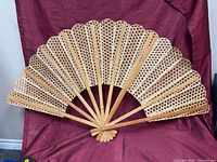 Full view of opened rattan cane weave fan against fabric backdrop