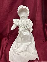 full front view of doll on stand in white gown and bonnet