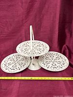 Stand fully opened displaying three circular floral cutout trays and carry handle with tape measure for scale
