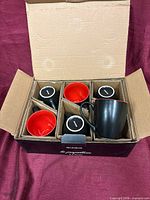 Box opened showing six mugs in cardboard dividers, brand name on box front