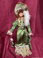 Full view of porcelain doll in green Victorian outfit on stand