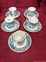 Five cup and saucer sets arranged on maroon cloth showing pattern