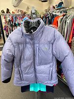 Front view of light purple The North Face puffer coat hanging