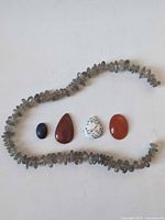 Full view of grey chip bead strand forming a loop around four cabochons