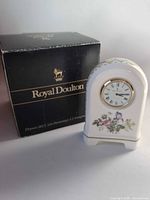 Front view of bone china clock beside branded box