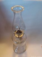 Full view of clear glass oil lamp with chimney