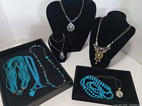 All eight light blue/turquoise necklaces displayed on trays and busts